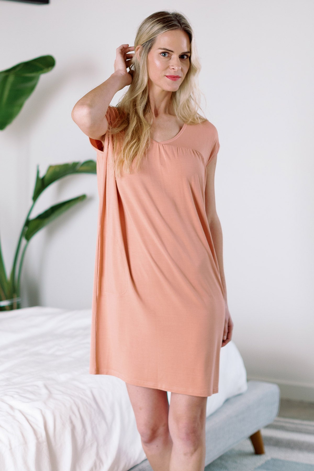 A woman standing with one hand raised to brush back her hair, wearing Yala Naomi V-Neck Babydoll Bamboo Nightgown in Apricot