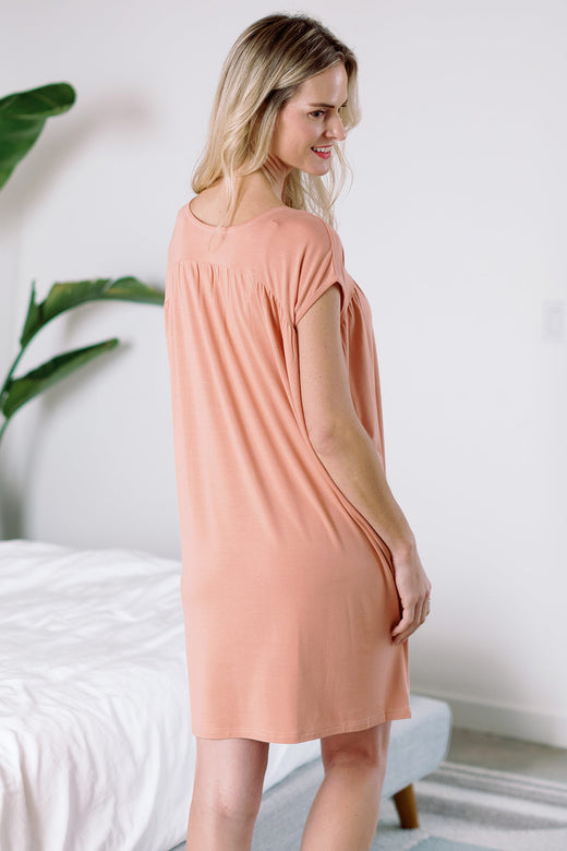 A woman standing facing away from the camera, looking back over her shoulder and smiling, wearing Yala Naomi V-Neck Babydoll Bamboo Nightgown in Apricot