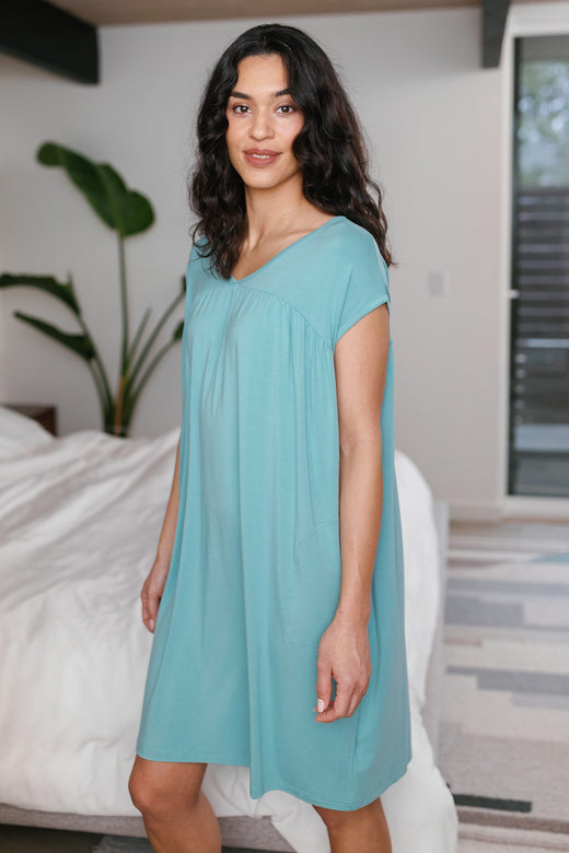 A woman standing facing partly to the side with one knee bent, wearing Yala Naomi V-Neck Babydoll Bamboo Nightgown in Nile