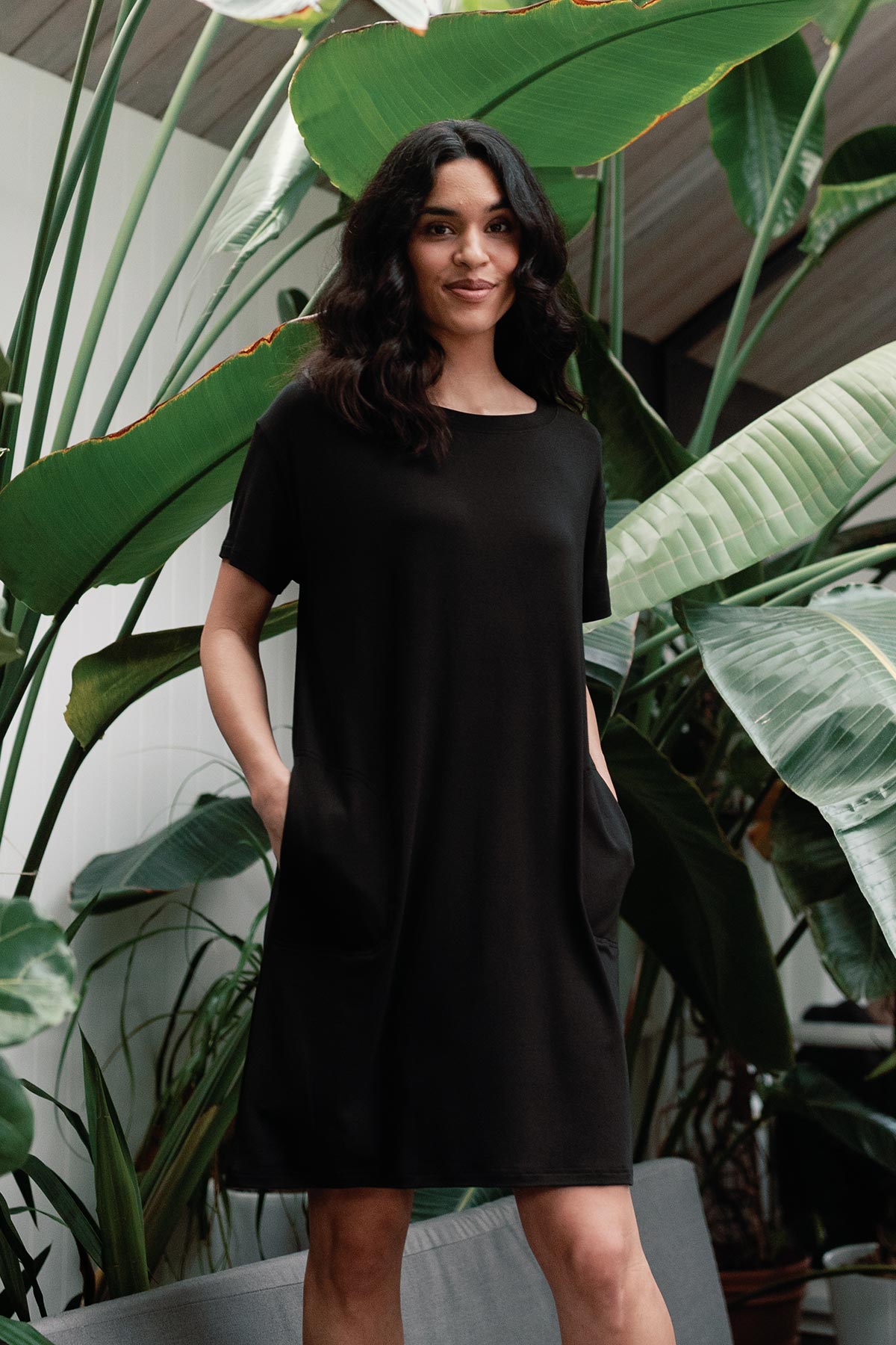 A woman standing with both hands in ther pockets, wearing Yala Reese T-Shirt Bamboo Shift Dress in Black