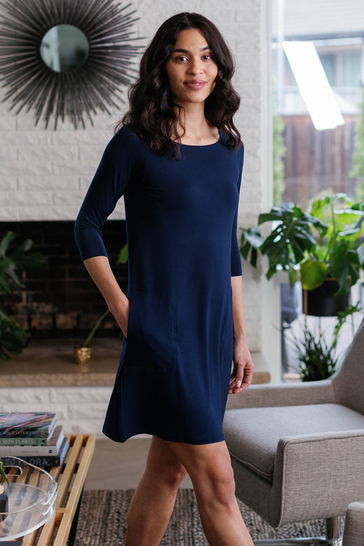 A woman striding to the side with one hand in her pocket, wearing Yala Rita Boatneck A-Line Bamboo Dress With Pockets in Navy