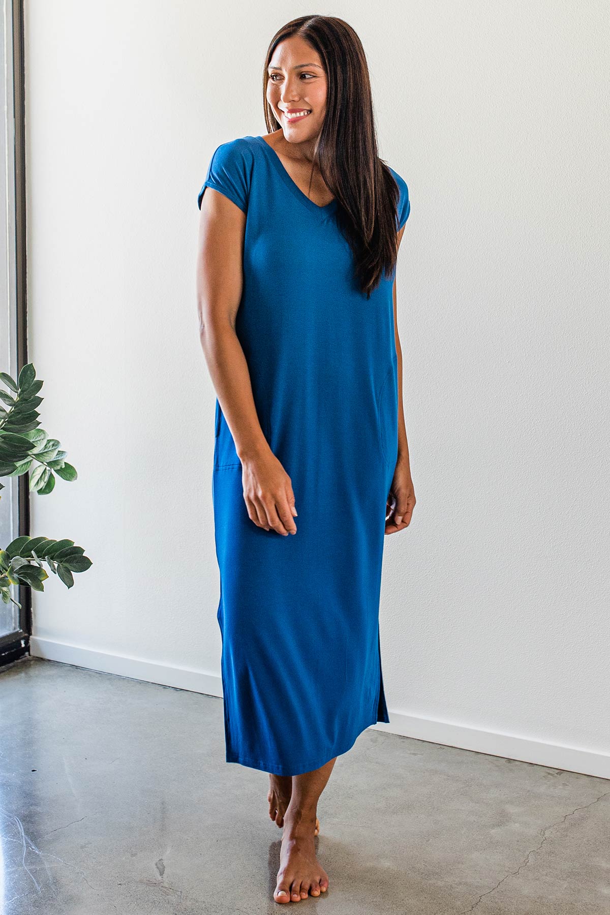A woman standing and smiling while looking to the side, wearing Yala Sloane V-Neck Cap Sleeve Bamboo Maxi Dress in Lapis